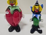 two figurines of clowns sitting on top of a red apple