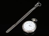 a silver pocket watch and a chain on a black surface