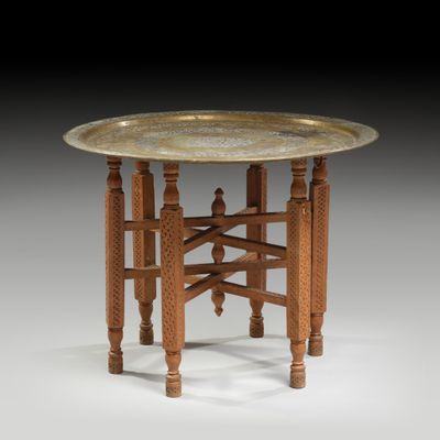 a brass plate topped table with wooden legs and a wooden base