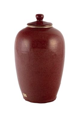 un vase rouge muni d'un couvercle, posé sur une surface blanche