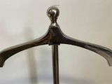 a silver coat hanger on a stand with a white wall in the background