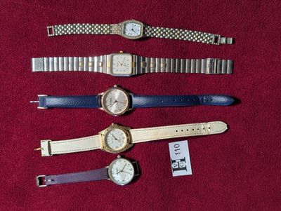 Plusieurs montres sont alignées sur un support rouge, accompagnées d'une étiquette de prix
