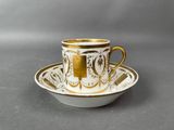 a white and gold cup and saucer on a gray surface