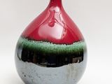 a red and green vase sitting on a white surface