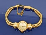 un bracelet en or sur lequel est fixée une montre, posé sur un fond bleu