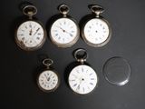 plusieurs montres de poche de différents types posées sur une table, à côté d'une loupe