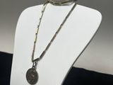 un mannequin blanc portant un collier sur lequel est accrochée une pièce de monnaie