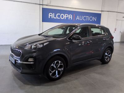 Une voiture grise est garée dans un garage où est accrochée une pancarte indiquant « Alcopa Auction ».