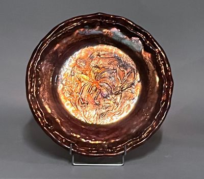 une assiette marron ornée d'un motif, posée sur un support