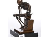 La statue d'un squelette est assise sur un bloc de bois.