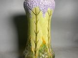 a green vase with purple flowers on it sitting on a table