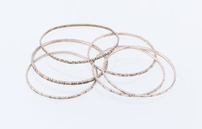 un gros plan sur une pile de bracelets en argent posés sur une surface blanche