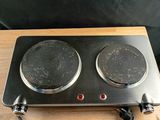 Deux réchauds sont posés sur une table en bois, sur fond noir.