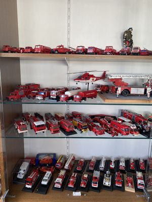 une vitrine remplie de camions de pompiers rouges et blancs et d'autres véhicules miniatures