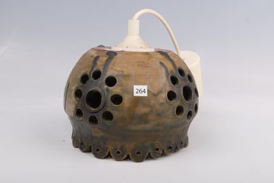un vase marron percé de trous posé sur une surface blanche