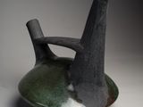 un vase noir et vert posé sur une surface blanche