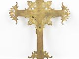 an antique brass cross on a stand against a white wall