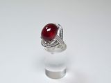 une image représentant une bague ornée d'une pierre rouge sur un support transparent
