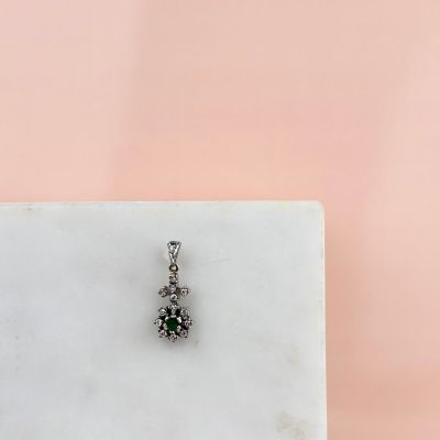 un gros plan d'un petit pendentif en forme de losange vert et blanc posé sur une surface en marbre blanc