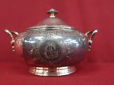 an antique silverplated bowl with a lid and handles on a red background