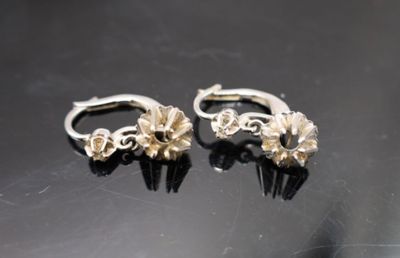 une paire de boucles d'oreilles en argent posées sur une surface noire, sur fond noir