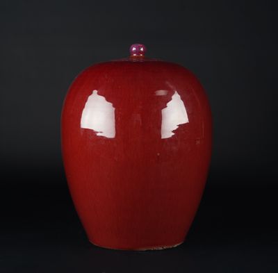 un vase rouge avec un couvercle rose posé sur une surface noire
