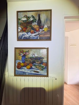 two paintings on the wall above a table with fruit