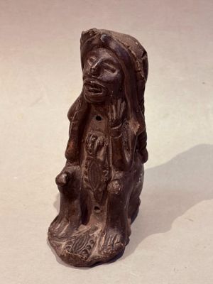 une vieille statue représentant une femme assise sur un rocher, posée sur un fond blanc