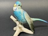 une figurine représentant une perruche bleue perchée sur une branche