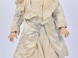 une poupée ancienne représentant une femme vêtue d'une robe blanche et d'un chapeau