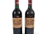 two bottles of red wine sitting next to each other on a white surface