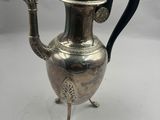 une théière ancienne en argent, avec une anse noire, posée sur un socle
