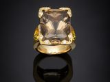 a yellow gold ring with a square faceted quartz stone on a black surface