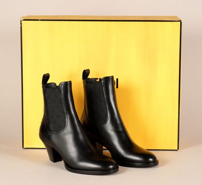 une paire de bottines en cuir noir devant une boîte jaune
