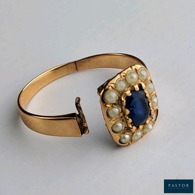 une image représentant une bague en or sertie d'une pierre bleue et entourée de perles