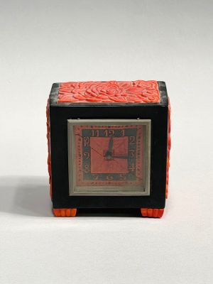 a small black and red clock sitting on a white surface