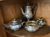 a silver tea set on a shelf in the corner of a cabinet