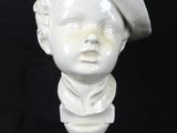 white marble bust of a boy wearing a hat on a marble base