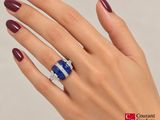woman ' s hand holding a blue and white diamond ring on a white background