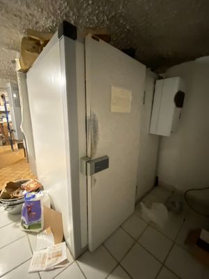 a white refrigerator in the corner of a room with a lot of clutter on the floor