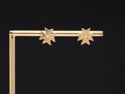 a pair of gold star earrings with diamonds on a black background