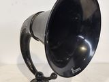 un vieux cor noir posé sur un support métallique, sur une surface blanche