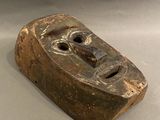 un vieux masque en bois posé sur une surface blanche
