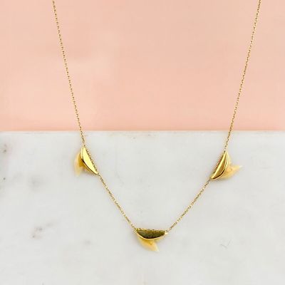 un collier plaqué or posé sur une surface en marbre, sur fond rose