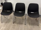 trois chaises en plastique noir sont alignées contre un mur blanc