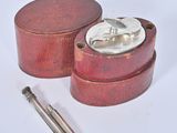 a small wooden box with a metal lid and a pen