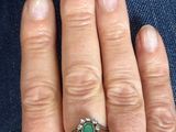 a woman ' s hand holding a ring with a green stone on it