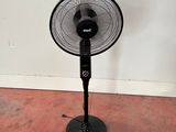 un ventilateur noir posé par terre devant un mur blanc