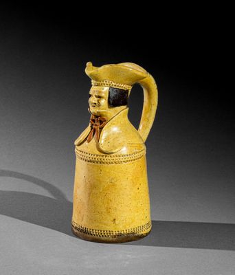 une vieille cruche jaune ornée d'une tête d'homme coiffée d'un chapeau