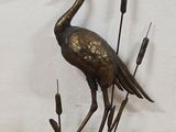 a bronze statue of a crane standing on a pond